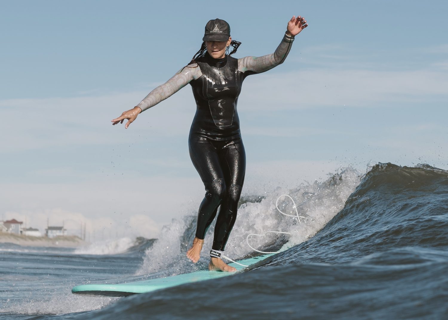 A surfer in an Outer Surf cap cruising on a teal longboard