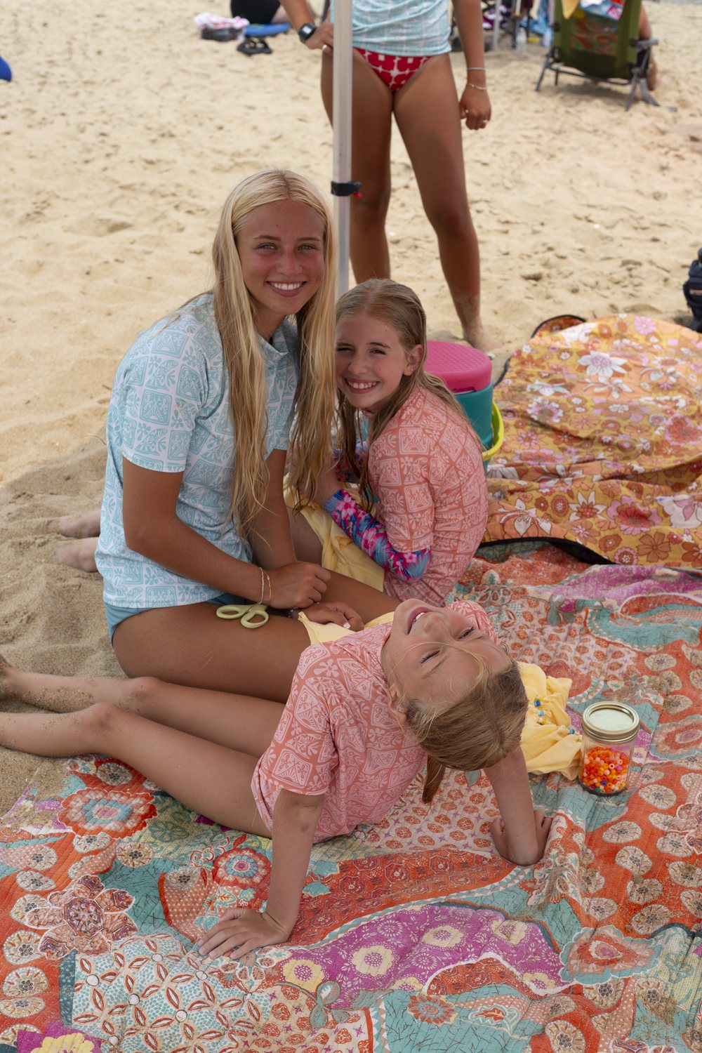 A teen instructor and two smiling campers on a beach blanket