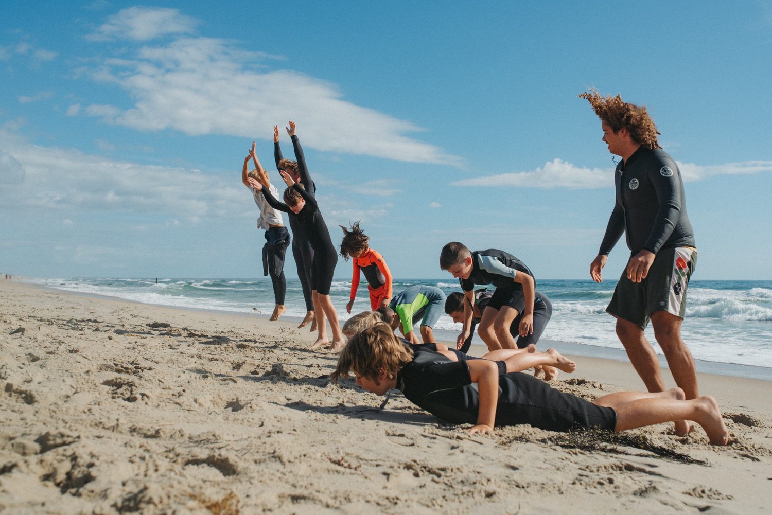 Boys camp groms practicing pop-ups on the sand with their instructor