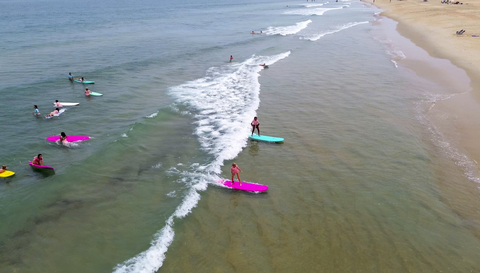 Campers catching waves on pink and teal soft-tops, seen from above