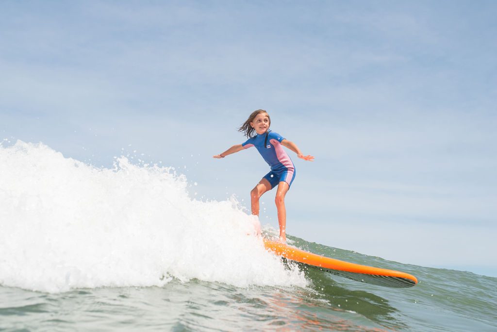 A young surfer riding an orange board through the whitewater