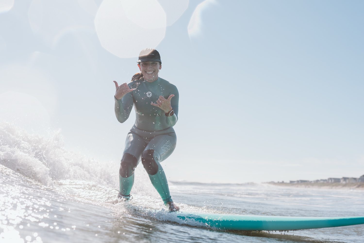 A smiling surfer throwing shakas while riding a teal board