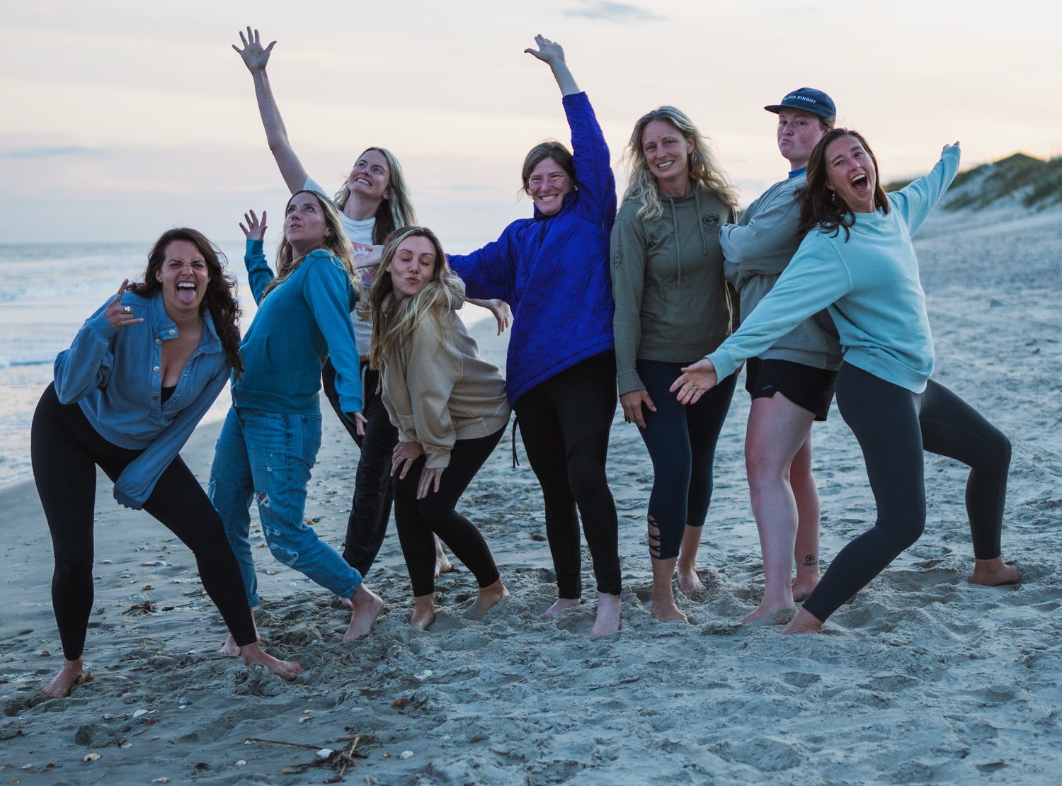 A group of women striking goofy poses on the beach at sunset