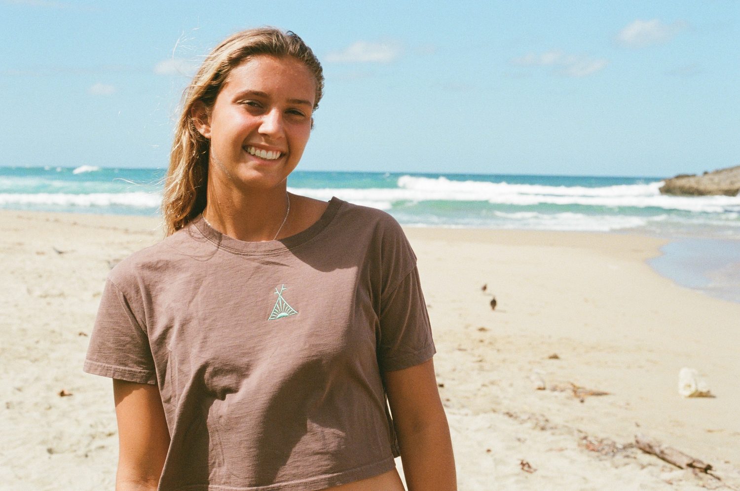A smiling teen surfer in an Outer Surf tee on the beach